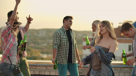 A-company-of-six-young-people-threw-a-party-on-the-roof.-This-is-dancing-fun-and-communication-between-friends-with-beer-in-plaid-shirts-and-shorts-in-the-summer.